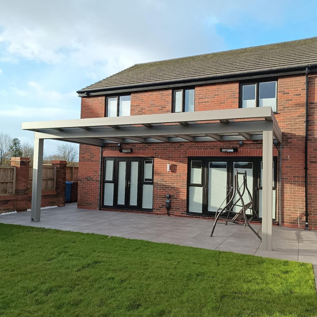 Silver-bronze aluminium veranda with a glass roof over a paved patio